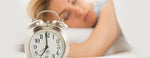 Mujer profundamente dormida con un reloj despertador en primer plano.